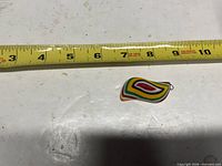 Front of pendant next to tape measure showing roughly 2 inch length with multicolor striped design and bail