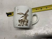 Front view of mug with hare graphic and measuring tape showing diameter and height