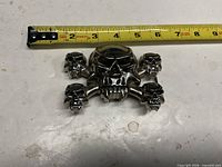 Front view of metal skull belt buckle next to tape measure
