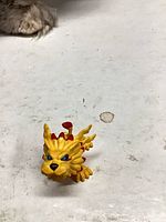 Front view of yellow plastic lion-like figurine with red accents and blue eyes