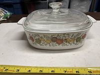 Front view of casserole with lid showing Spice of Life pattern and measuring tape for size reference