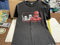 Front view of black Star Wars Stormtroopers graphic T-shirt with measuring tape showing size