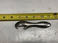 Top view of bottle opener beside tape showing length