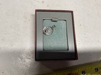 Toronto metal charm in presentation box, measuring tape in foreground