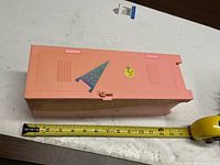 Closed pink locker with decals beside tape measure ~10"