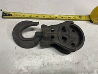 Top view of cast iron farm pulley showing hook marked B7, wheel and body, tape measure for scale