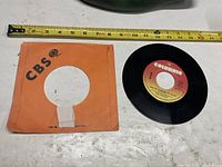 Vinyl record and orange CBS sleeve beside measuring tape