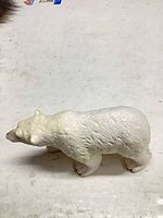 Side profile of white plastic polar bear figurine showing overall form and texture