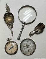 Group view of two compasses, magnifier, tea strainer and sugar scoop