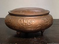 Side view of copper vessel showing embossed decoration and tripod feet