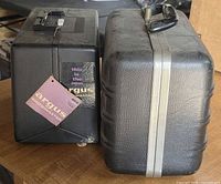 Two black projector carrying cases, left labeled Argus Showmaster, right unlabeled