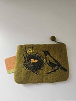 Front view showing bird, nest graphic, zipper with pom pull, attached tags