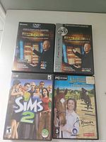 Four PC game cases laid out; two Deal or No Deal copies, The Sims 2, Alexandra Ledermann