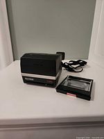 Polaroid Sun 600 LMS camera closed with film cartridge beside