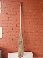 Full view of entire wooden canoe paddle front against brick wall