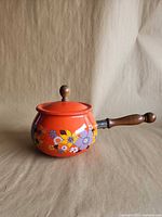 side view of orange floral fondue pot with lid and wood handle