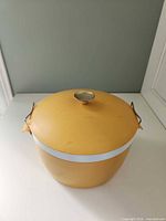 Front view of mustard yellow insulated serving dish with lid and wire side latches
