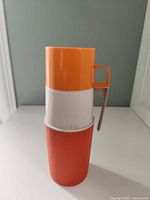 Front view of orange and white Thermos with lid and handle