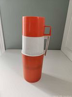 Full view of assembled orange and white Thermos showing handle and cup lid