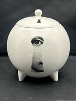 Front view of white spherical ceramic diffuser jar with keyhole eye motif and tripod feet