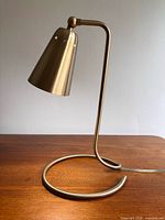 Full view of brushed brass desk lamp showing loop base and cone shade