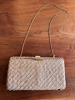 Front view of woven straw box clutch showing chain strap and clasp