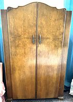 Front view of burl walnut armoire showing doors, veneer, brass pulls, arched crown