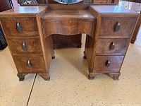 Front view of walnut burl vanity table showing seven drawers, brass pulls, kneehole design, and feet