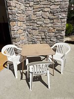 Square tan vinyl folding card table with three white plastic chairs