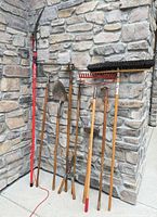 group shot of all long-handled tools leaning against stone wall