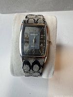 Front view of Coach rectangular wristwatch on display pillow showing dial and fabric strap