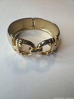 Overall view of gold-tone chunky equestrian bit bangle showing clasp and link design
