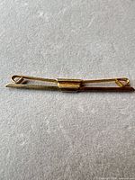 Full view of gold tone tie clip on grey surface