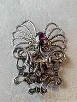 Front view of ornate silver-tone brooch with purple glass stone and pin closure