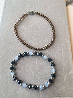 Overhead view of two bracelets: brown faceted glass bead line bracelet with silver-tone tube clasp and blue stretch beaded bracelet with navy, pale blue and silver-tone beads