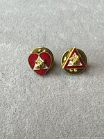 Front view of both enamel lapel pins showing heart and triangle shapes with handshake emblems