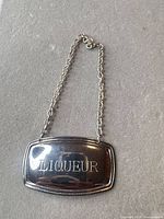 Front view of silver-plated decanter label showing engraved text and chain