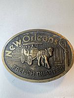 Front view of brass oval belt buckle with horse-drawn carriage design and New Orleans French Quarter text