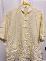 Front view of yellow Tang jacket on hanger showing frog closures and pockets