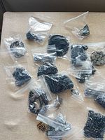 Overview of multiple small bags containing black and silver jewelry pieces and bead lots