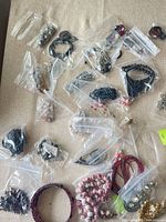 Overview of clear bags containing various jewelry pieces and beads on fabric surface