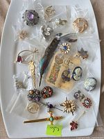 Overhead shot of approx. 18 vintage brooches and pins bagged on white tray