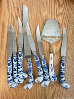 Full set of eight cheese knives and server showing Delft style handles and stainless blades