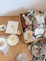 Overview of unwrapped dinnerware, coin bank, book, and box containing wrapped pieces
