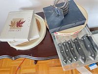 All boxed items together including knife set blister pack, boxed cheese set, ceramic plate, cork trivet