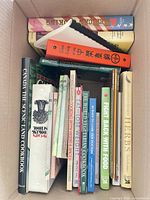 Top-down view of box containing 14 assorted cookbooks of various sizes and bindings