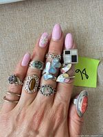 Hand wearing ten sterling silver rings displaying various cabochon and inlay gemstones
