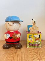 Charlie Brown ceramic cookie jar next to Snoopy tin jack-in-the-box with puppet extended