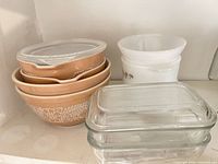 stacked tan floral mixing bowls with clear lids, white milk glass ramekins, clear refrigerator dish with lid