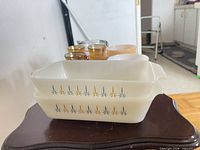 Stacked Pyrex rectangular dishes showing atomic starburst decals; background glimpse of other glassware